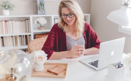 woman smiling holding glass mug sitting beside table with MacBook